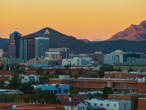 Wide view of the University of Arizona campus with mountains and a sunset in the background.