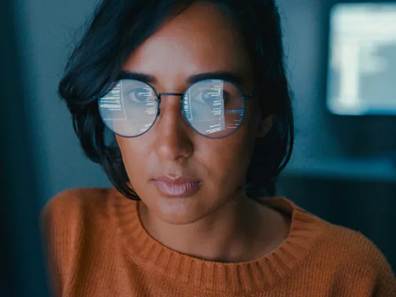 A woman using a computer with text on the screen reflected in her eyeglasses.