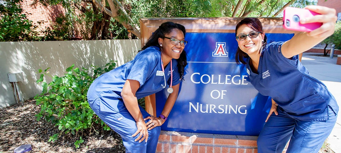 Two female students taking a selfie in front of the University of Arizona College of Nursing sign