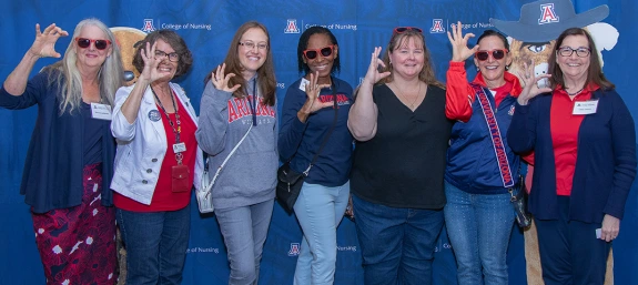 Seven alumni standing infront of U of A background giving the wildcat hand sysmbol