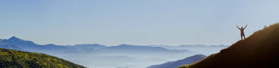 Man on hill with arms raised to sky