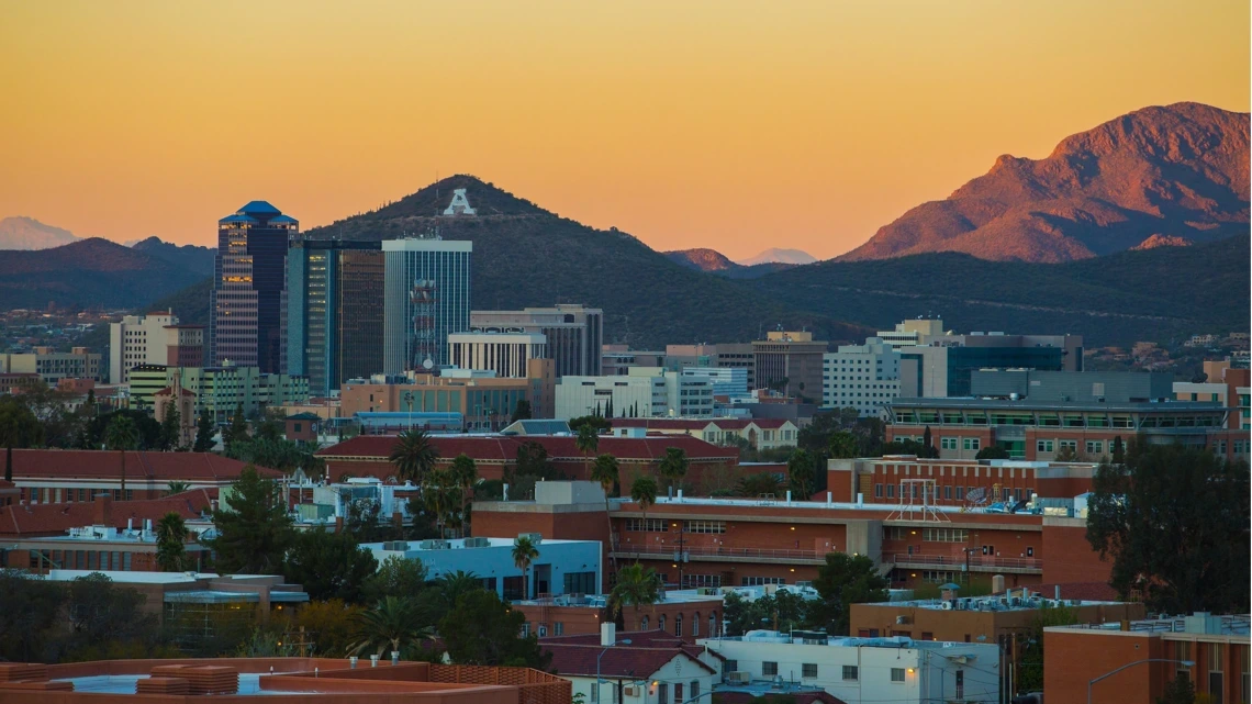 Wide view of the University of Arizona campus with mountains and a sunset in the background.