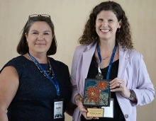 Head and shoulders shot of Jen Bea and Rina Fox holding her award.
